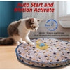 A gray and white cat is interacting with a round, patterned mat designed to activate a motion-sensitive toy.