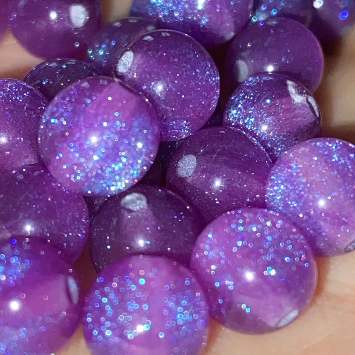 A close-up of small, iridescent purple resin spacer beads with a starry glitter finish.