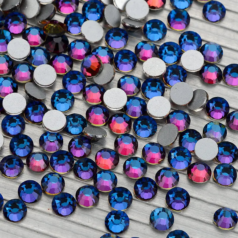 A collection of iridescent glass crystal flatback rhinestones in various shades of blue, purple, and pink.