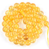 A string of small, round, translucent yellow-orange beads made from natural sea sediment jasper and turquoise for jewelry mak