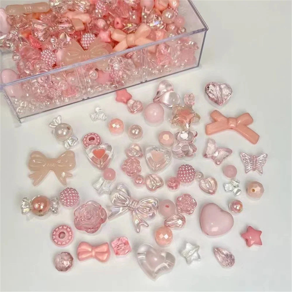 A collection of pink and clear acrylic bow and flower beads for jewelry making displayed in a clear box.