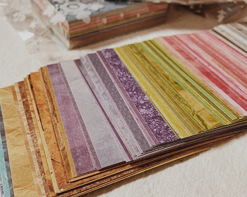 A close-up of a stack of rainbow textured paper sheets in various shades and stripes.