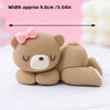 A cute, round brown bear cake topper with pink accents is shown on a white surface.