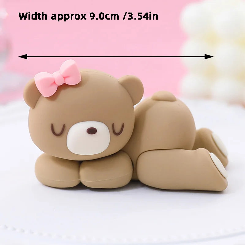 A cute, round brown bear cake topper with pink accents is shown on a white surface.