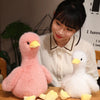 A woman holds a pink plush duck toy and a white plush duck toy on a wooden surface.