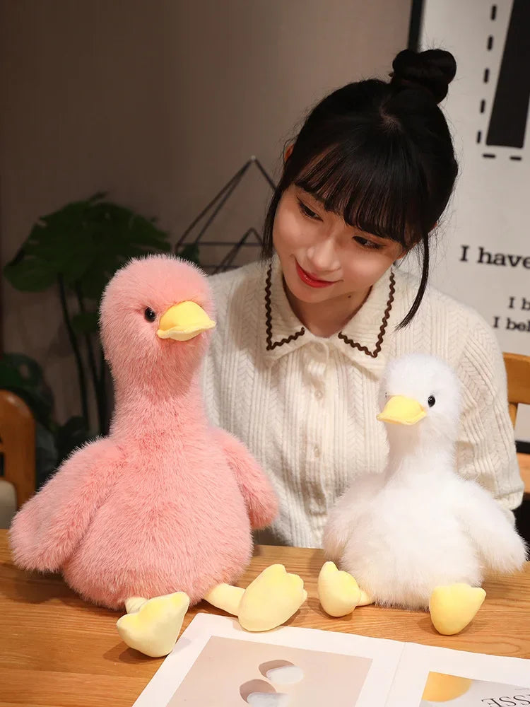 A woman holds a pink plush duck toy and a white plush duck toy on a wooden surface.