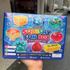 A box of Squishy Fun Box sensory toys including a cheese cube, snowflake cube, ocean cube, bread, and apple.