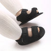 Black breathable first walker sandals for baby with hook-and-loop closure shown on a foot wearing a white sock.