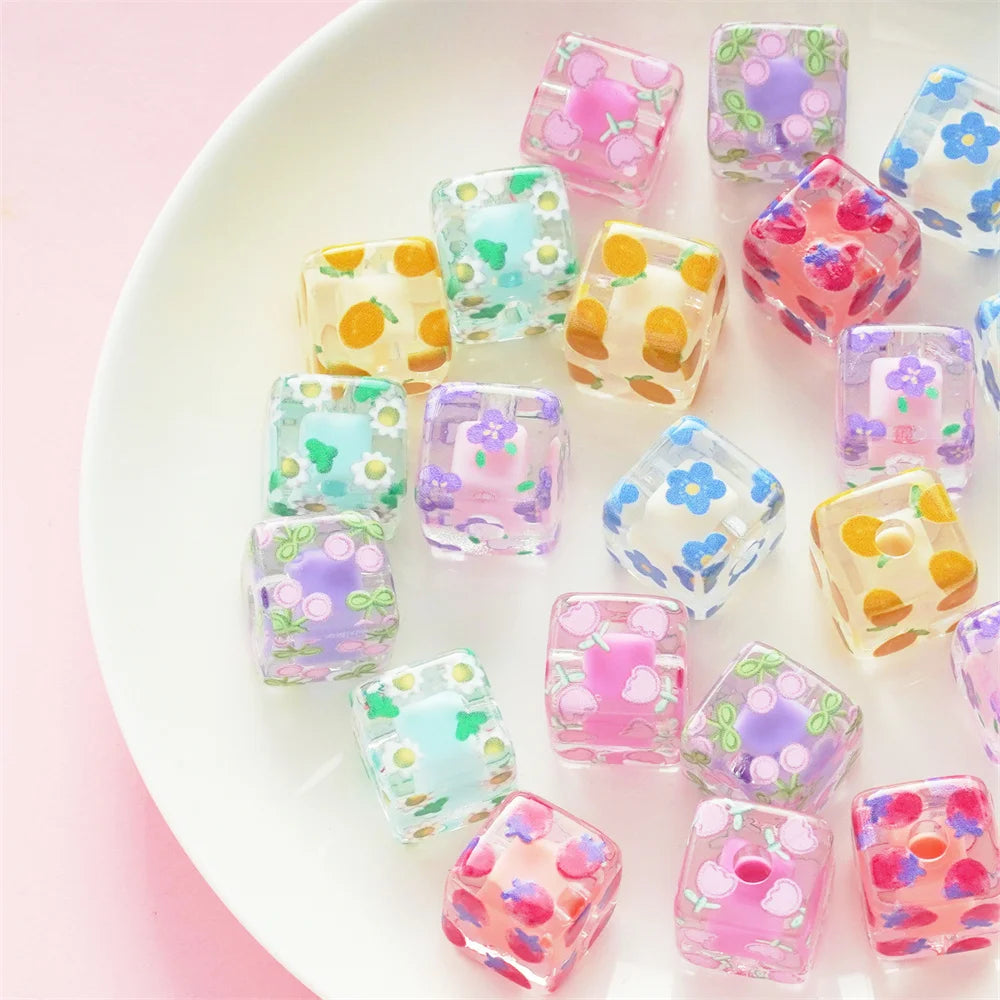 A collection of colorful floral square resin beads in various shades of pink, purple, and green on a white plate.