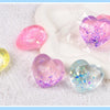 A collection of iridescent heart-shaped squishy toys in pink, yellow, and blue colors resting on a white surface.