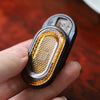 A hand holds a black metal mechanical fidget slider with an amber gem design.
