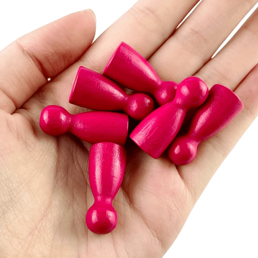 A hand holds a set of twelve wooden game pawns in six vibrant shades of pink and magenta.