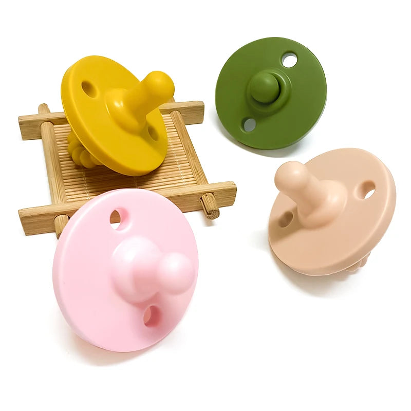 Tres chupetes o supedores de silicona para bebé en amarillo, verde y rosa exhibidos sobre una superficie de madera.