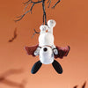 A white Snoopy collectible figure with brown ears and a red cape is suspended from bare branches against an orange background