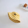 A yellow and white checkerboard bucket hat is displayed on a white surface next to a book.