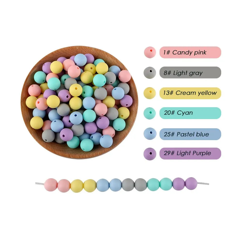A collection of colorful silicone round beads in pink, gray, yellow, and blue shades arranged on a wooden plate.