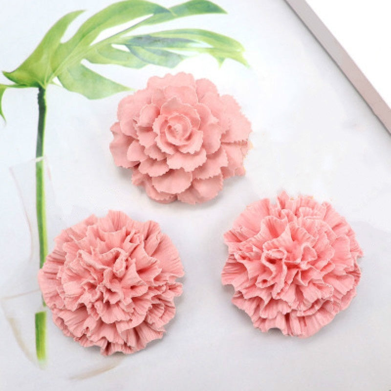 Pink ruffled 3D flower silicone mold for soap, candle, and cake decorating placed on a white surface with green leaves.