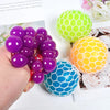 A hand holds purple and blue squeeze stress relief balls with mesh netting against a floral background.