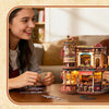 Three people interact with a wooden 3D puzzle music box model kit on a table.
