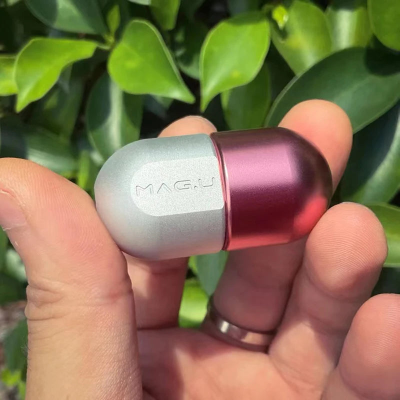 A hand holds a metallic pink and silver magnetic levitating fidget slider device against a blurred green leaf background.