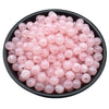 A pile of pink translucent acrylic round beads for jewelry making in various sizes.