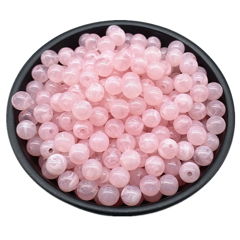 A pile of pink translucent acrylic round beads for jewelry making in various sizes.