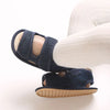 A pair of navy blue breathable first walker sandals for a baby, shown on a leg.