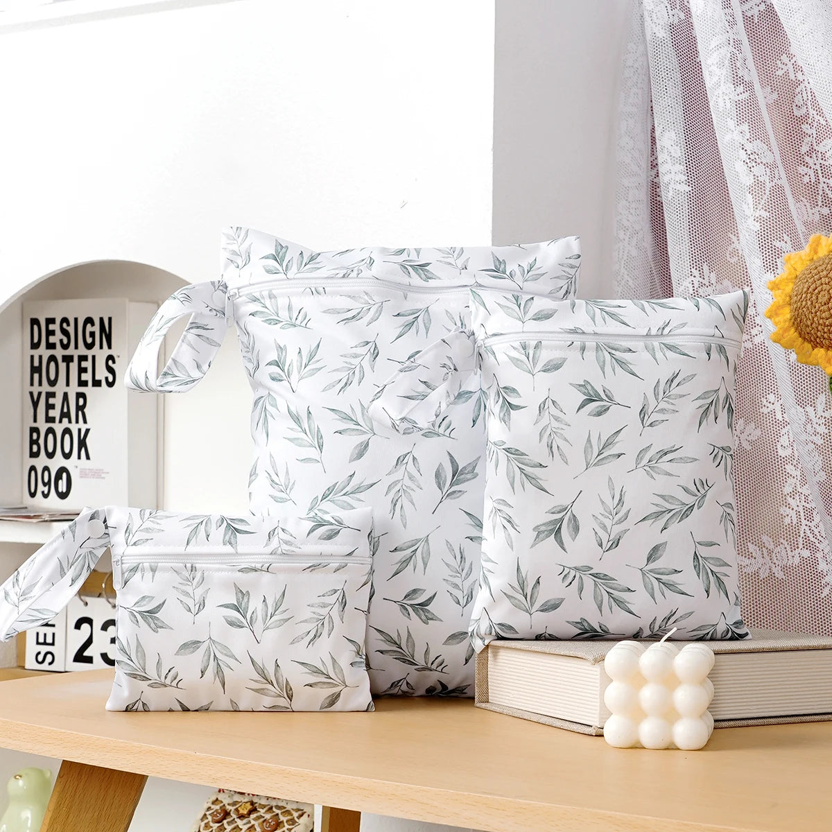 A set of three white waterproof bags featuring a green leaf pattern, displayed on a wooden surface.