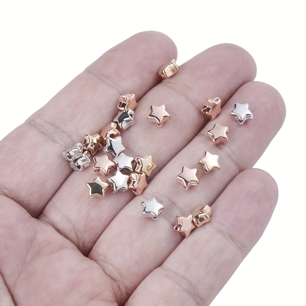 A hand holds various acrylic star and heart spacer beads for jewelry making in gold and silver tones.