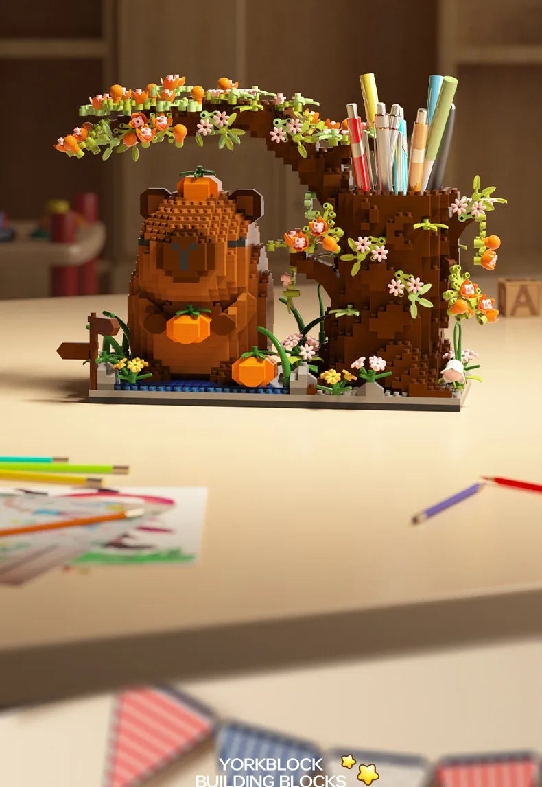 A terracotta building block capybara figurine with foliage and an orange pumpkin, used as a desk organizer.