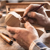 Hands are carving a piece of wood using a pencil on a basswood carving block.
