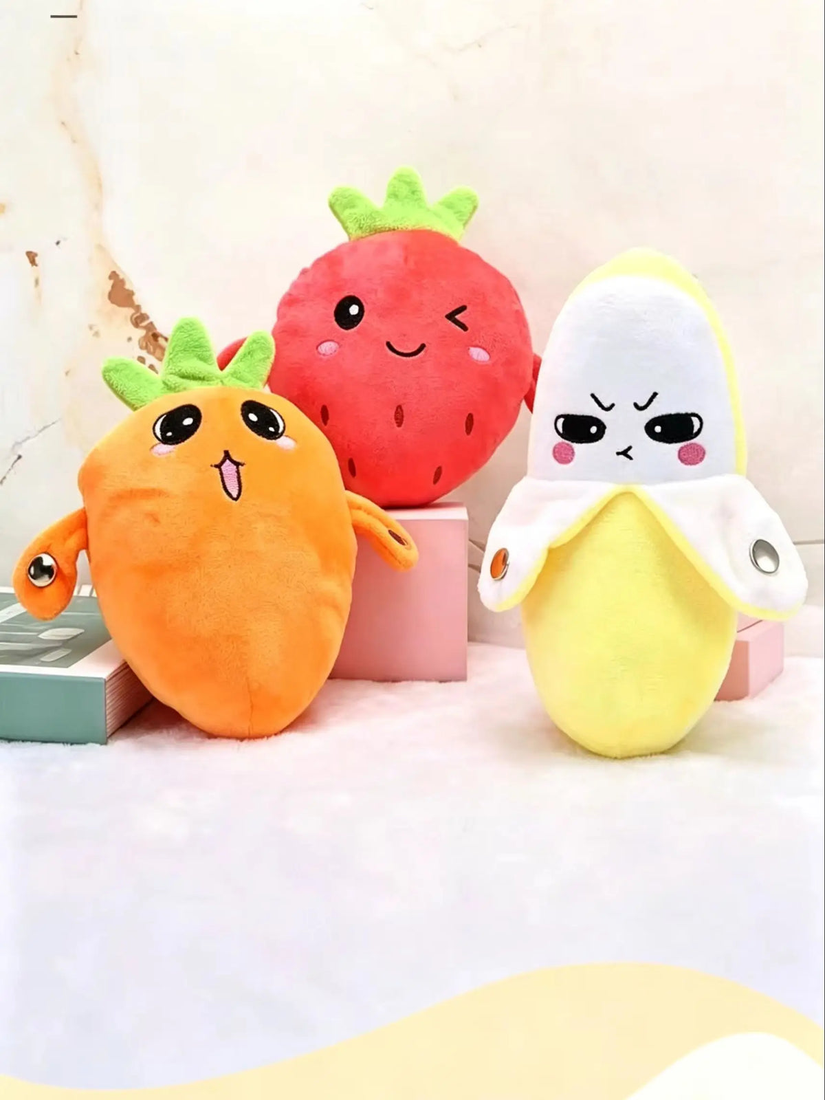 Three plush toys shaped like a strawberry, a carrot, and a banana with faces.