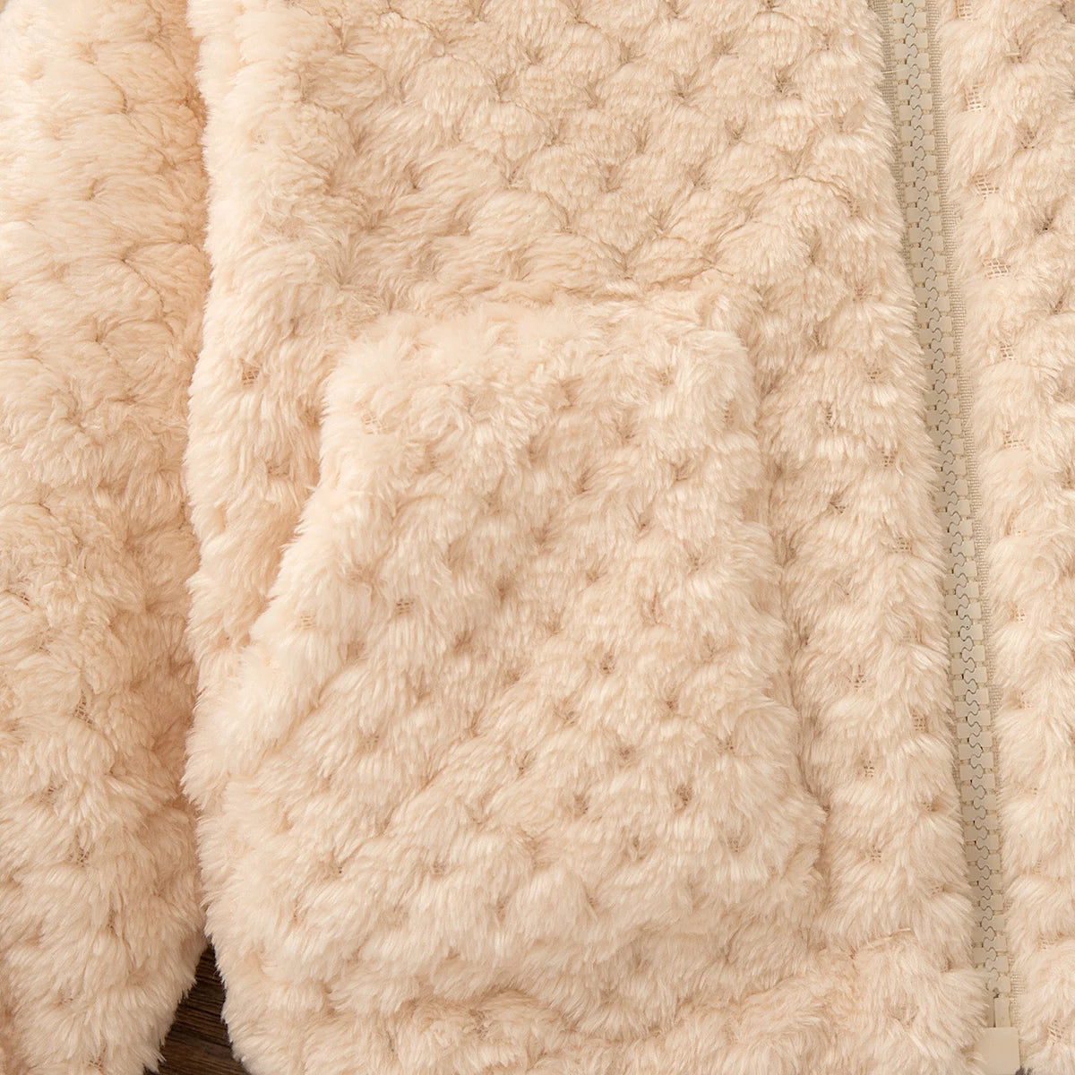 A close-up of a light beige plush hooded winter jacket with a visible seam detail.