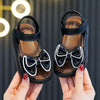 A pair of black and white bow detail breathable summer sandals being held by a person.