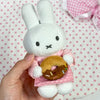 A white bunny plush toy with pink clothing and a golden donut charm is held in a hand.