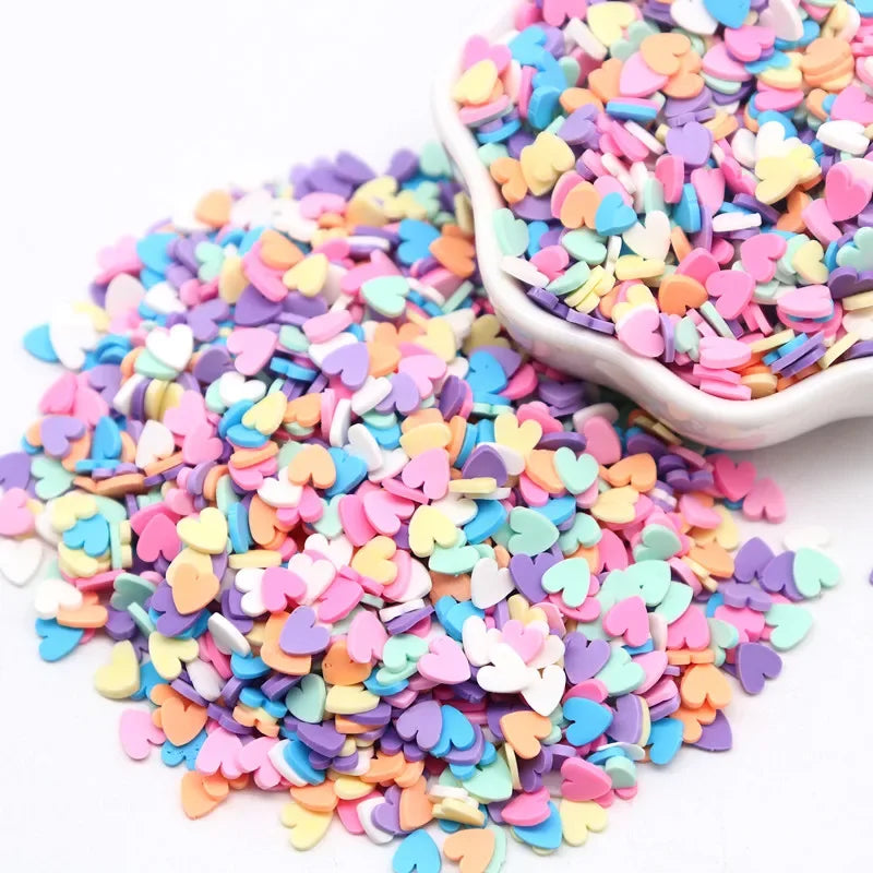 A pile of colorful polymer clay sprinkles in various shades of pink, purple, and yellow hearts.