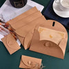 A stack of mini kraft paper envelopes with heart clasps in various shades of brown resting on a green surface.