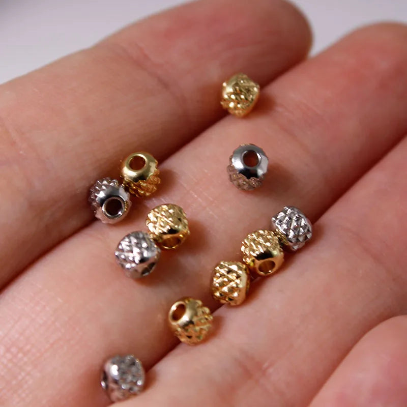 A hand holds various gold and silver stainless steel round spacer beads for jewelry making.