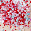 A colorful mix of red, pink, and blue resin rhinestones and pearls with an AB finish scattered on a light wooden surface.