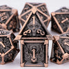 A close-up of a brass and black metal dice set featuring skull and dragon designs for tabletop role-playing games.