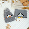A gray knit penguin hat and matching scarf set with white accents resting on a white surface.