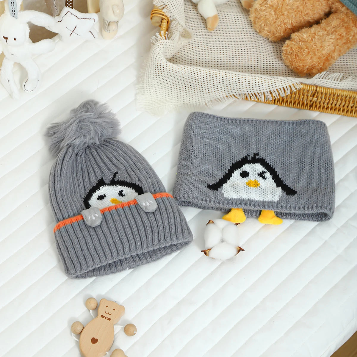 A gray knit penguin hat and matching scarf set with white accents resting on a white surface.