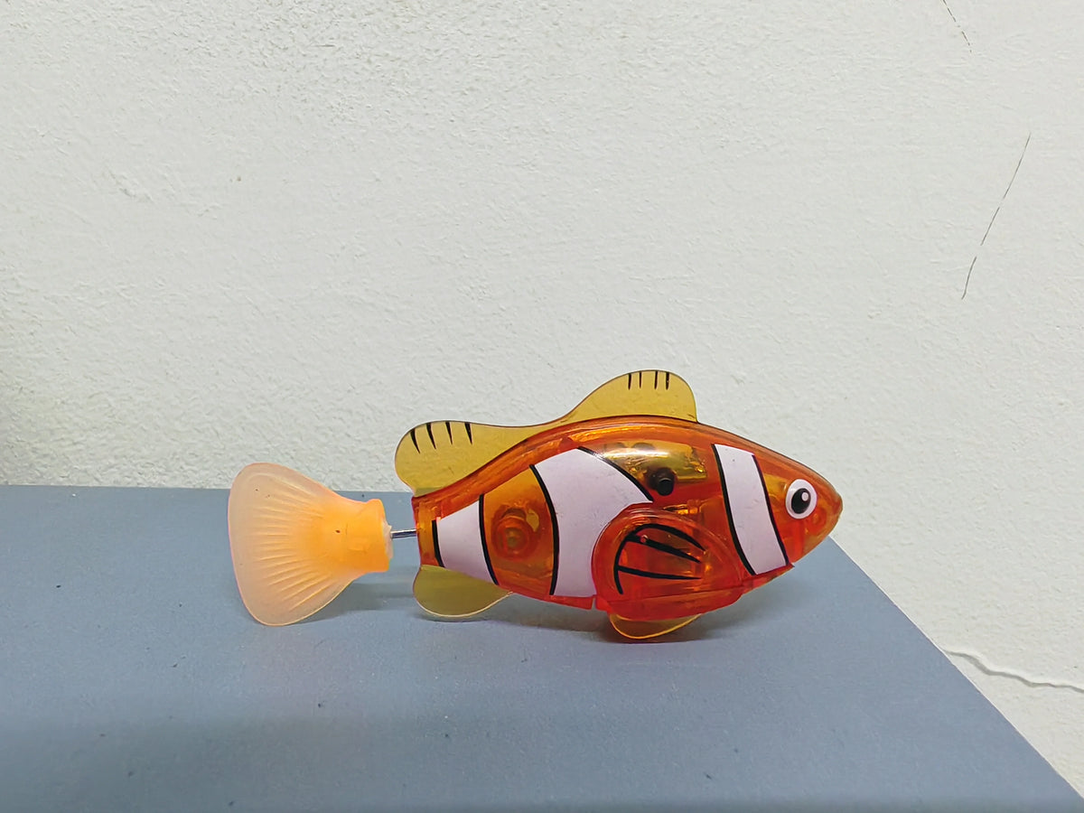 An orange and white light-up bath toy shaped like a fish with a translucent yellow trumpet.