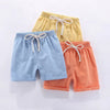 Three pairs of kids cotton-linen summer shorts in yellow, light blue, and coral orange with adjustable elastic waists