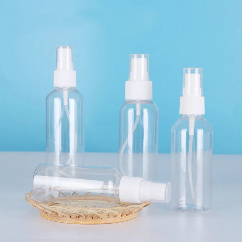 Three clear refillable travel spray bottles with fine mist pumps displayed on a light blue background.