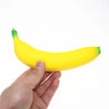 A hand is holding a bright yellow squishy banana stress relief toy.