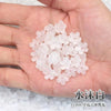 A hand holds a pile of clear pink sakura flower crystal glass beads for jewelry making.