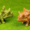 A small green dinosaur fossil model is placed on bright green textured surface.
