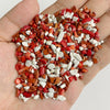 A hand holds a pile of natural tumbled stone chips in various shades of red, orange, and white.