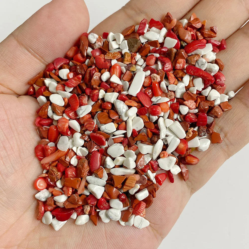 A hand holds a pile of natural tumbled stone chips in various shades of red, orange, and white.